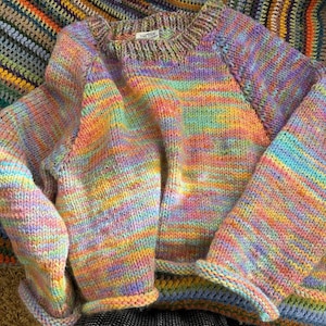 May include: A multi-coloured striped knitted jumper with a crew neck and long sleeves. The jumper is made of a soft, fuzzy yarn and has a relaxed fit.