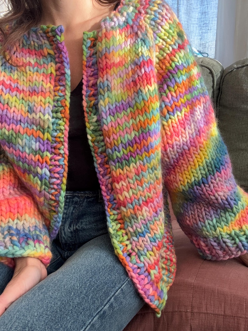 May include: A chunky knit cardigan in a vibrant rainbow of colors, including pink, orange, yellow, green, and blue. The open-front sweater features long sleeves and a thick, textured knit, perfect for adding a pop of color to any outfit.