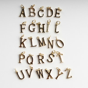 May include: Gold-coloured alphabet charms, each with a small loop for attaching to a chain or bracelet. The letters A to Z are displayed, ideal for personalised jewellery. The charms are arranged on a white surface.