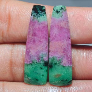Op de afbeelding: Twee langwerpige, taps toelopende edelsteen cabochons met een opvallende kleurencombinatie van levendig magentarood-roze en diep bosgroen. De stenen vertonen een natuurlijke, gevlekte textuur met kristallijne patronen en donkere insluitingen.