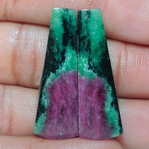 Peut inclure: Deux pierres précieuses trapézoïdales en vrac présentant un centre magenta vibrant entouré d'inclusions minérales vert foncé et noires. Les pierres ont une surface lisse et polie avec un dégradé de couleurs distinct allant du cœur rose aux bords sombres.