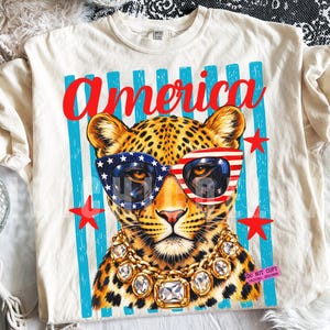 Patriotic leopard PNG design featuring glamorous leopard wearing American flag sunglasses and chunky gold jewelry on retro blue striped background. Trendy USA coquette animal graphic perfect for 4th of July shirts, patriotic apparel, summer vacation tees, western glam fashion, Independence Day party outfit, leopard lover gift, sublimation PNG, DTF transfer, print on demand design, tumbler wrap, mug design, wall art printable, boutique graphic tee, trendy Americana aesthetic clipart.