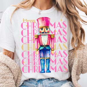 Hand-painted watercolor nutcracker soldier Christmas PNG design in vibrant pink, gold, and blue with festive stars and layered “Merry Christmas” lettering. Perfect for holiday shirts, Christmas party outfits, Nutcracker ballet gifts, winter home décor, festive wall art, seasonal apparel, cozy holiday decorations, and Christmas gift ideas for women and kids.