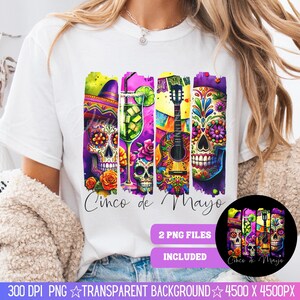 May include: A white t-shirt with a colorful graphic design featuring a guitar, a glass of margarita, and sugar skulls. The graphic is surrounded by a purple, yellow, and green border. The text "Cinco de Mayo" is written below the graphic.