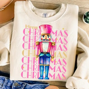 Hand-painted watercolor nutcracker soldier Christmas PNG design in vibrant pink, gold, and blue with festive stars and layered “Merry Christmas” lettering. Perfect for holiday shirts, Christmas party outfits, Nutcracker ballet gifts, winter home décor, festive wall art, seasonal apparel, cozy holiday decorations, and Christmas gift ideas for women and kids.