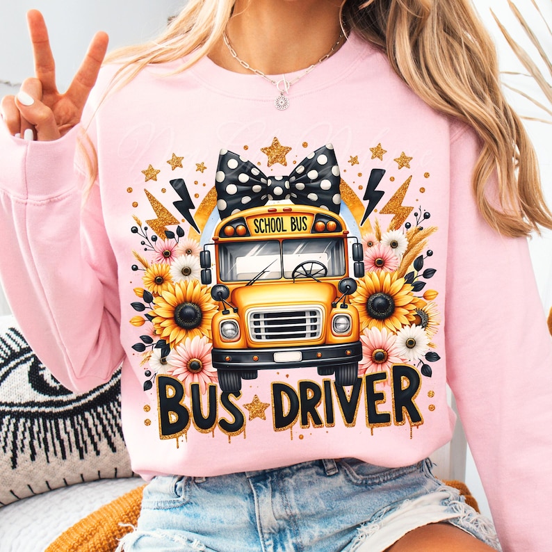 May include: Pink sweatshirt with a yellow school bus graphic, a black and white polka dot bow, and the text "BUS DRIVER" in black with gold glitter accents.