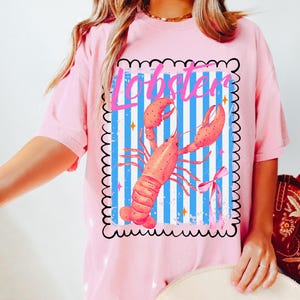 Bold watercolor lobster design with pink bow on nautical blue and white stripes — perfect for coastal cowgirl aesthetic, seafood lovers, Maine lobster festival gifts, retro summer beach vibes, ocean-themed apparel, and girly cottagecore fans. Trendy crustacean print for quirky fashion, East Coast preppy style, Y2K nautical chic, or seaside travel souvenir. Great for lobster parties, boating outfits, or colorful graphic tees with a fun foodie twist.