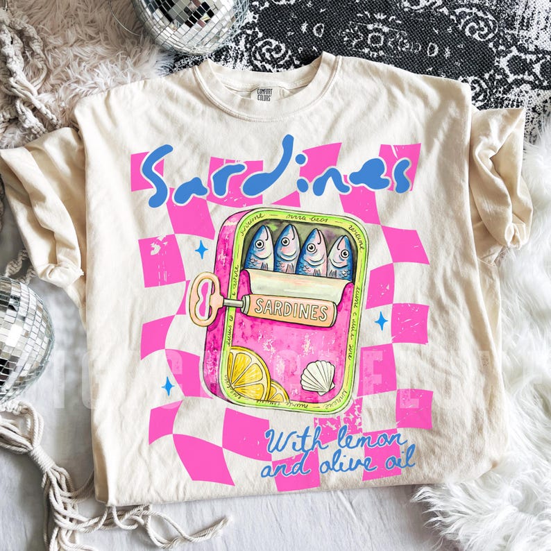 Trendy sardines shirt design featuring a pink illustrated sardine tin can with fish, lemon slices, shell detail, blue lettering, and hot pink checkerboard background. Cute Mediterranean foodie graphic perfect for coastal Europe vacations, European summer outfits design, fish market aesthetic, seafood lover gifts, retro vacation shirts design, beach trip apparel design, coastal boutique fashion, and trendy graphic shirt design for women, girls trips, and summer travel. For sublimation and DTF.