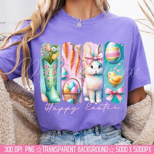 May include: Purple t-shirt with a graphic design of a bunny, a boot, carrots, eggs, and a chick. The graphic has a distressed look and the text "Happy Easter" is printed below the design.