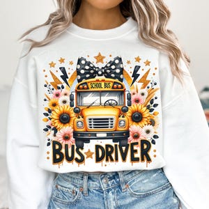 May include: White sweatshirt with a yellow school bus graphic, black and white polka dot bow, and the text "Bus Driver" in gold glitter. The bus has the words "School Bus" on the front.