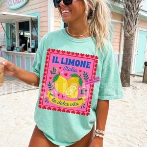 Pink Italian lemon shirt PNG design featuring bold yellow lemons, heart scalloped border, “Il Limone Italia” and “La Dolce Vita” text in retro Mediterranean style. Amalfi Coast aesthetic graphic tee design, lemoncore fashion, Italian summer shirt design, Italy vacation shirt, cute Europe travel apparel, feminine coastal citrus art, Italy lover gift, Lemon wall art, Mediterranean fruit illustration PNG clipart design.