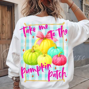 May include: White sweatshirt with a colorful graphic of pumpkins and the text "Take me to the pumpkin patch." The design features a yellow bow, a light blue gingham background, and orange star accents.