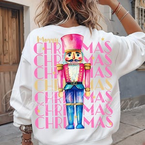 Hand-painted watercolor nutcracker soldier Christmas PNG design in vibrant pink, gold, and blue with festive stars and layered “Merry Christmas” lettering. Perfect for holiday shirts, Christmas party outfits, Nutcracker ballet gifts, winter home décor, festive wall art, seasonal apparel, cozy holiday decorations, and Christmas gift ideas for women and kids.