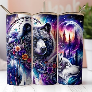 May include: Three stainless steel tumblers with different designs. The first tumbler features a black bear with a dreamcatcher and flowers. The second tumbler features a black bear with flowers and a purple background. The third tumbler features a wolf with a moon and forest background.