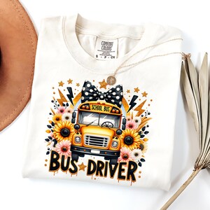 May include: A white t-shirt with a yellow school bus graphic, sunflowers, and a black and white polka dot bow. The text "School Bus" and "Bus Driver" are printed on the shirt.