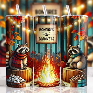 Puede incluir: Un vaso de acero inoxidable con un diseño otoñal caprichoso. El vaso presenta mapaches con bufandas, una hoguera y el texto "Bonfires & Blankets". El diseño incluye hojas de otoño y luces de cadena, creando un tema acogedor y de temporada.