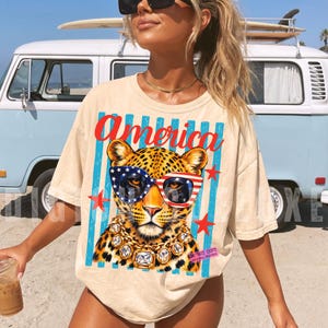 Patriotic leopard PNG design featuring glamorous leopard wearing American flag sunglasses and chunky gold jewelry on retro blue striped background. Trendy USA coquette animal graphic perfect for 4th of July shirts, patriotic apparel, summer vacation tees, western glam fashion, Independence Day party outfit, leopard lover gift, sublimation PNG, DTF transfer, print on demand design, tumbler wrap, mug design, wall art printable, boutique graphic tee, trendy Americana aesthetic clipart.