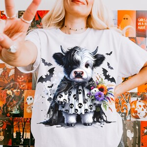 Adorable baby Highland cow in a black skull cape and spooky dress, holding a colorful fall bouquet with a skull plush. This cute Halloween cow PNG design is perfect for sublimation, fall clipart, kids Halloween shirt designs, printable wall art, spooky cute decor, cow lover gifts, and gothic autumn apparel. Great for tees, sweaters, mugs, and farmhouse Halloween crafts.