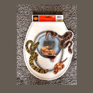 Könnte beinhalten: Ein weißer Toilettensitzbezug mit einem Grafikdruck von mehreren Schlangen in verschiedenen Farben und Mustern, darunter Gelb, Braun und Orange, die ein zentrales Abflussloch umgeben. Die Verpackung zeigt ein Kürbis-Symbol und den Text Creepy Toilet Cover.