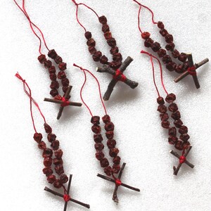 以下が含まれることがあります： 乾燥したベリーと小枝で作った手作りクリスマスオーナメント5個。各オーナメントには赤い紐と小枝の十字架が付いています。