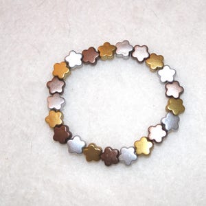Könnte beinhalten: Ein Armband aus kleinen, sternförmigen Perlen in Silber, Gold und Bronze.