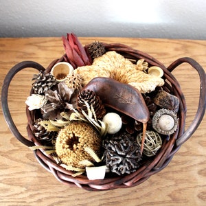 May include: A brown wicker basket with two handles filled with dried natural elements, including pinecones, dried flowers, and a brown seed pod.