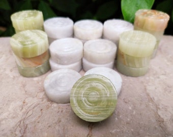 May include: A set of 14 green and white marble game pieces. The pieces are round and have a slightly raised center. They are arranged in a circle on a light brown surface.