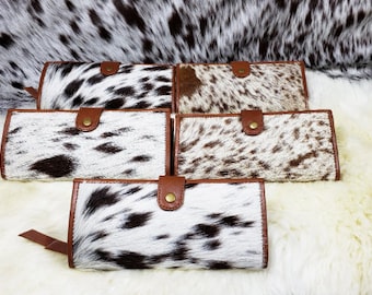 May include: Five brown and white cowhide wallets with brown leather trim and a brass snap closure.