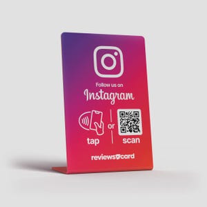 Può includere: Un cartello rettangolare con un gradiente da viola a rosso. Presenta il logo di Instagram, il testo "Follow us on Instagram" e le opzioni per "toccare" o "scansionare" un codice QR per connettersi.
