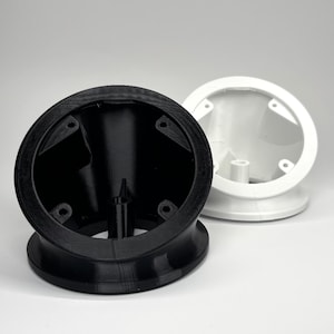 May include: Two 3D-printed objects, one black and one white, are displayed against a white background. The objects have a circular design with a flared base and a central cylindrical component. The black object is in the foreground, with the white object slightly behind it.