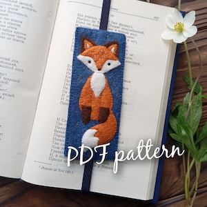 May include: A PDF pattern for a felt fox bookmark. The bookmark is blue with a felt fox in orange, brown, and white. The fox is standing on its hind legs with its tail curled around its body.