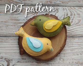 May include: Two felt bird ornaments, one yellow with a blue wing and one green with a yellow wing, on a wooden slice. The text "PDF pattern" is written above the birds.