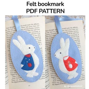 May include: Two felt bunny bookmarks are displayed on open book pages. One has a blue dress, the other a red jacket. The bookmarks are light blue ovals with white bunny figures. The image text reads "Felt bookmark PDF PATTERN".