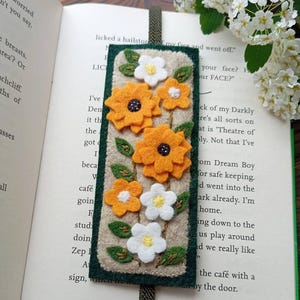 Puede incluir: Un marcapáginas de fieltro hecho a mano con aplicaciones de flores naranjas y blancas y hojas verdes. El marcapáginas rectangular tiene un borde verde y una cinta verde oscuro. El texto "PDF PATTERN" está en la parte superior y "Instant Download" en la inferior.