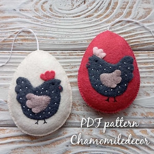May include: Two felt Easter egg decorations featuring a black and white chicken design. One egg is white and the other is red. The eggs have a loop for hanging. The text "PDF pattern Chamomiledecor" is at the bottom of the image.
