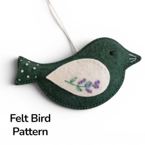 May include: A dark green felt bird ornament with a white wing patch featuring purple floral embroidery. The bird has a black eye, white stitched details on the tail, and a white hanging string. The text Felt Bird Pattern is visible below.