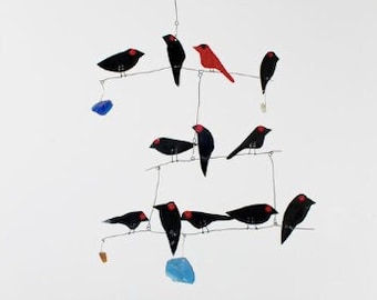 May include: A mobile with black and red birds hanging from a wire frame. The birds are painted with black and white details. There are blue and brown accents hanging from the bottom of the mobile.