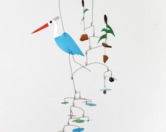 May include: A blue and white bird mobile with brown and green accents. The mobile is suspended from the ceiling and features a bird with a long beak and a long tail. The mobile also features several small, round shapes in various colors.