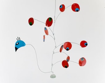 May include: A mobile sculpture with a blue bird head and red circular shapes with black and green eyes. The mobile is suspended from the ceiling with thin wires.
