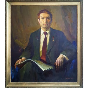 Puede incluir: Una pintura al óleo en un marco dorado que representa a una persona de cabello castaño corto con traje oscuro, camisa blanca y corbata roja. La persona lleva un pequeño broche de estrella dorada en la solapa y sostiene papeles en las manos.