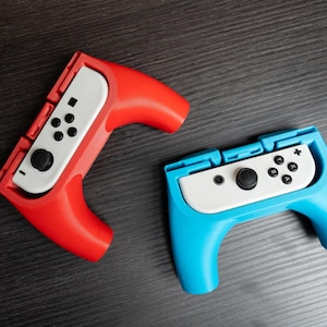 May include: Two Nintendo Switch Joy-Con controllers, one red and one blue, with white buttons and a white faceplate. The controllers are designed for handheld gaming.