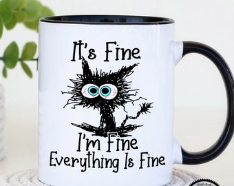 May include: White ceramic mug with a black rim and handle. The mug features a black and white illustration of a cat with the text "It's Fine I'm Fine Everything Is Fine".