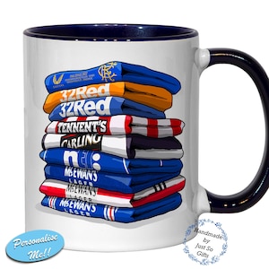 Peut inclure: Mug en céramique blanche avec intérieur et anse bleu marine. La tasse présente une pile de maillots de football bleus, rouges et blancs avec des logos de sponsors. Le mug a le texte "Personalise Me!!" et "Handmade by Just So Gifts".