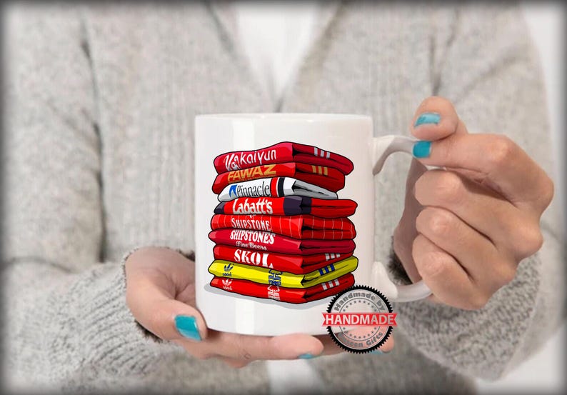 K&ouml;nnte beinhalten: Wei&szlig;e Keramiktasse mit einem bunten Design aus &uuml;bereinander gestapelten Hockeytrikots mit verschiedenen Markennamen, darunter "Kaltyn", "Fawaz", "Pinnacle", "Labatt's", "Shipstone", "Skoal" und "Handmade Gifts".