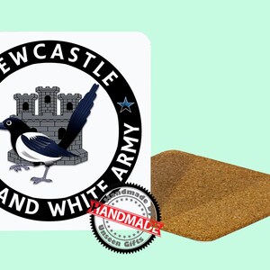 May include: A white square sticker with a black and white magpie bird illustration, the words "NEWCASTLE BLACK AND WHITE ARMY" in a circle, and a cork coaster. The sticker has a castle illustration and star accents. The coaster is rectangular.