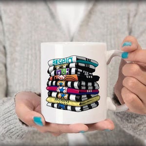 K&ouml;nnte beinhalten: Wei&szlig;e Keramiktasse mit einem bunten Stapel bedruckter Fu&szlig;balltrikots. Die Trikots sind schwarz, wei&szlig;, blau, rot, gelb und gr&uuml;n. Die Tasse hat einen schwarzen Henkel.