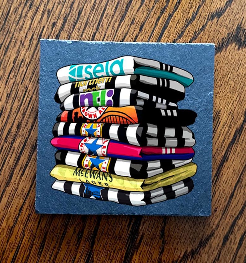 May include: A stack of colorful, folded t-shirts with various logos and text, including "Kisela" and "MCEWANS LAGER". The shirts are primarily black and white striped, with accents of teal, orange, pink, and yellow. The shirts are stacked on a square, blue-gray surface.