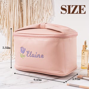 May include: A pink, faux leather makeup bag with a bow detail and a zipper closure. The bag is 9.45 inches wide, 5.91 inches long, and 5.32 inches tall. The bag has the name "Elaine" embroidered on the front in purple thread.
