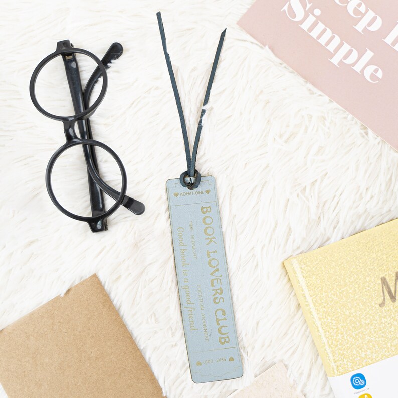 May include: A blue and white bookmark with the text "Book Lovers Club" and the quote "Good book is a good friend." The bookmark is attached to a black string.
