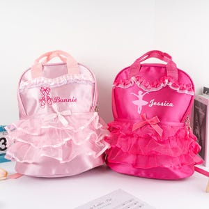 May include: Two pink and fuchsia ballerina backpacks with tulle ruffles. The pink backpack has a ballerina shoe design and the text "Bonnie". The fuchsia backpack has a ballerina silhouette and the text "Jessica".